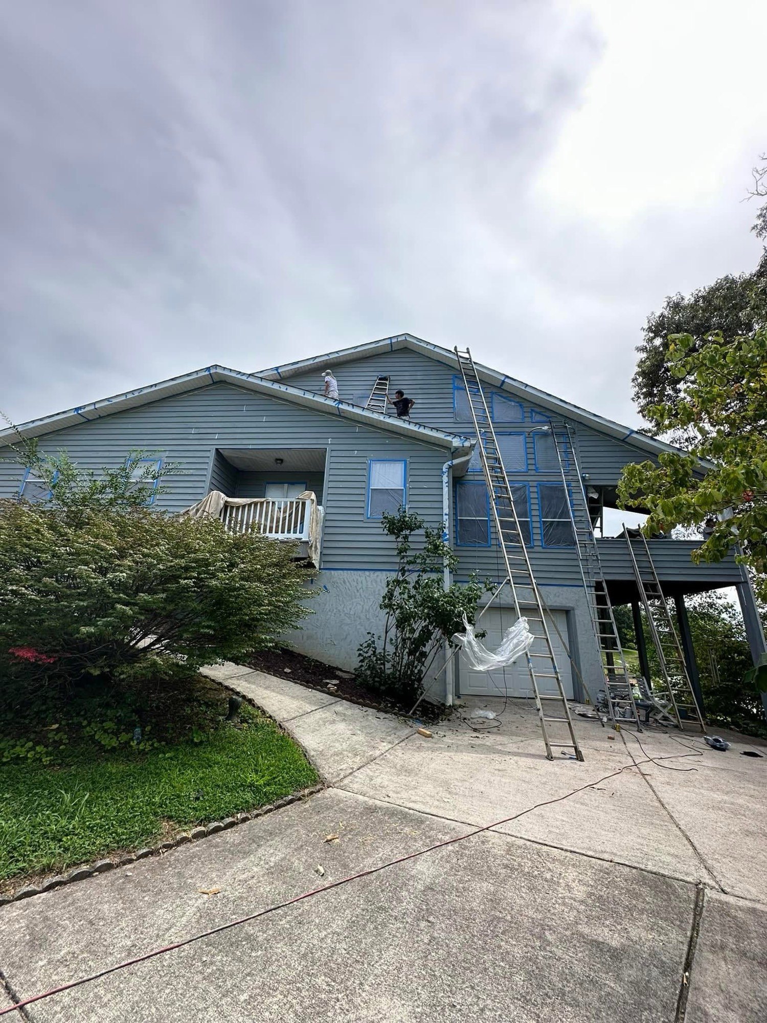 Two-story house mid-paint with ladders and crew on the roof